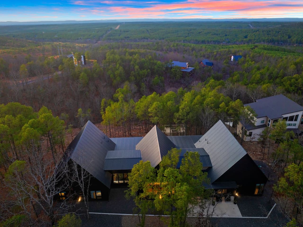 This modern home tucked into the forest with those dramatic angular roofs and glowing windows is basically the kind of architectural statement that makes you feel like you've discovered something really special hidden away in the pines.