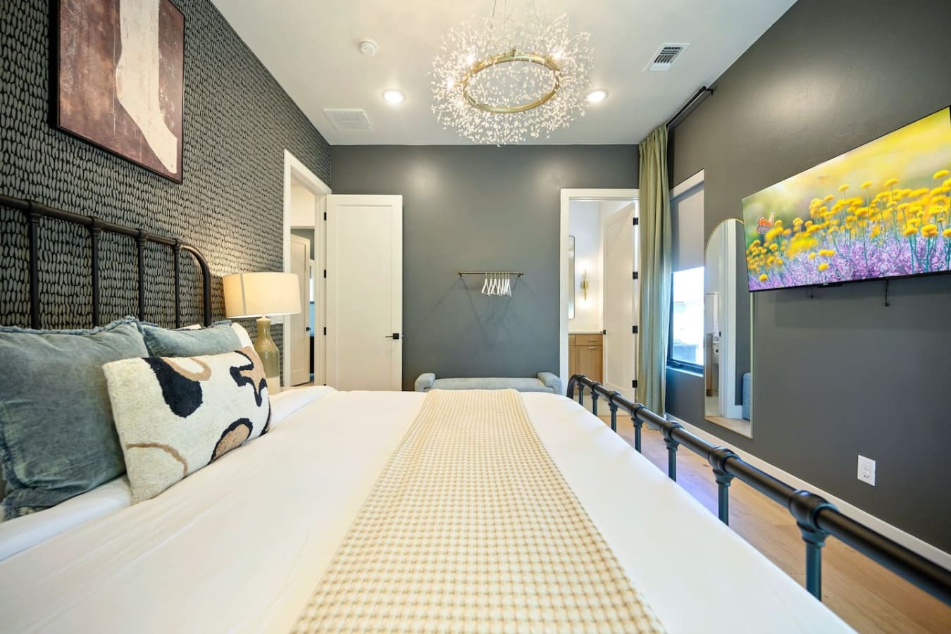 This master bedroom is basically a serene escape with those soft gray walls, that elegant black metal bed frame, the gorgeous crystal chandelier catching the light just right, and floor-to-ceiling windows that let you drift off watching the treetops.