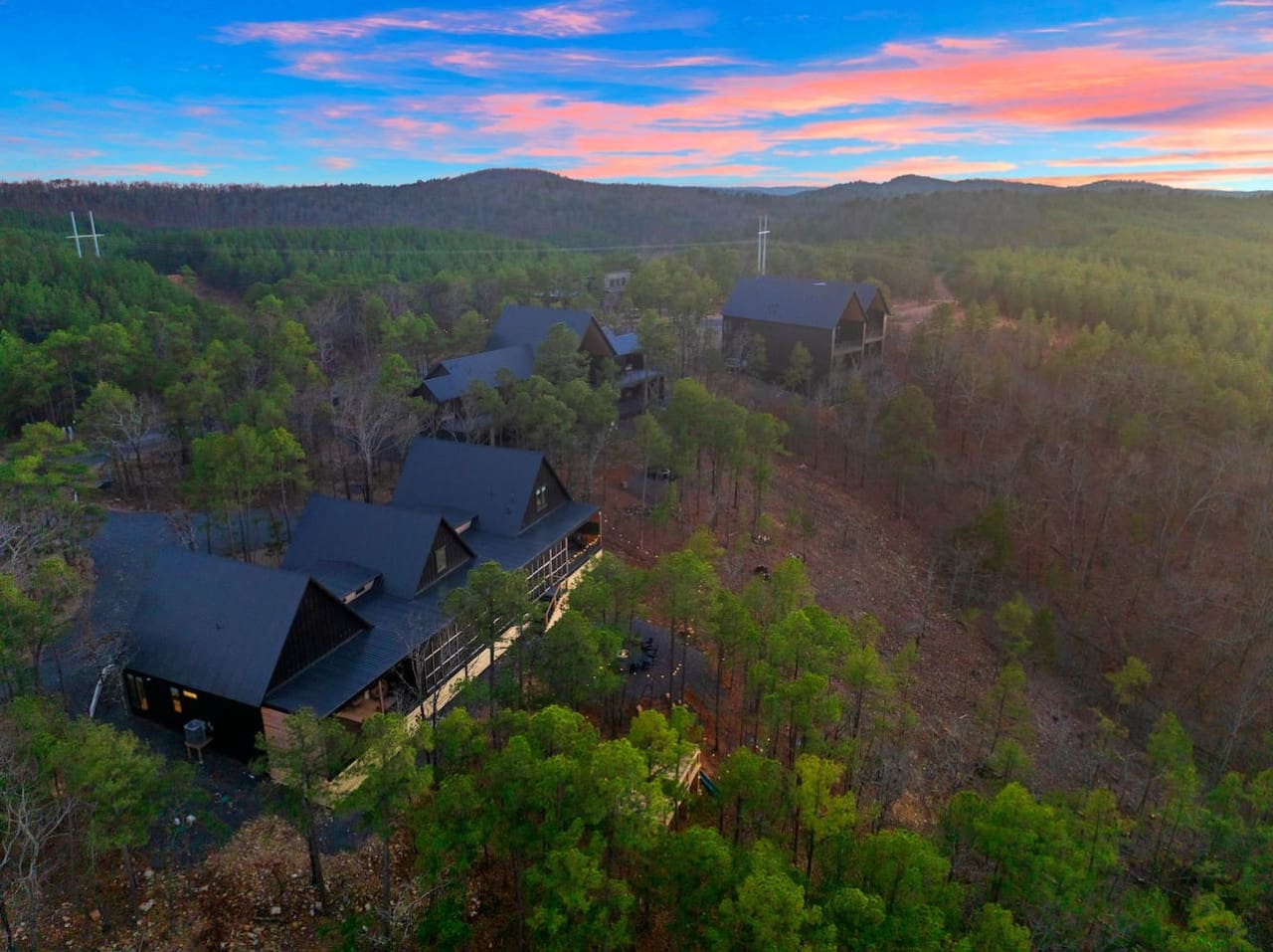 Imagine waking up to this view—a stunning architectural retreat nestled in the pines with those dramatic roofs and glowing windows, surrounded by endless forest and mountains in the distance, basically the kind of hidden gem where nature and modern design
