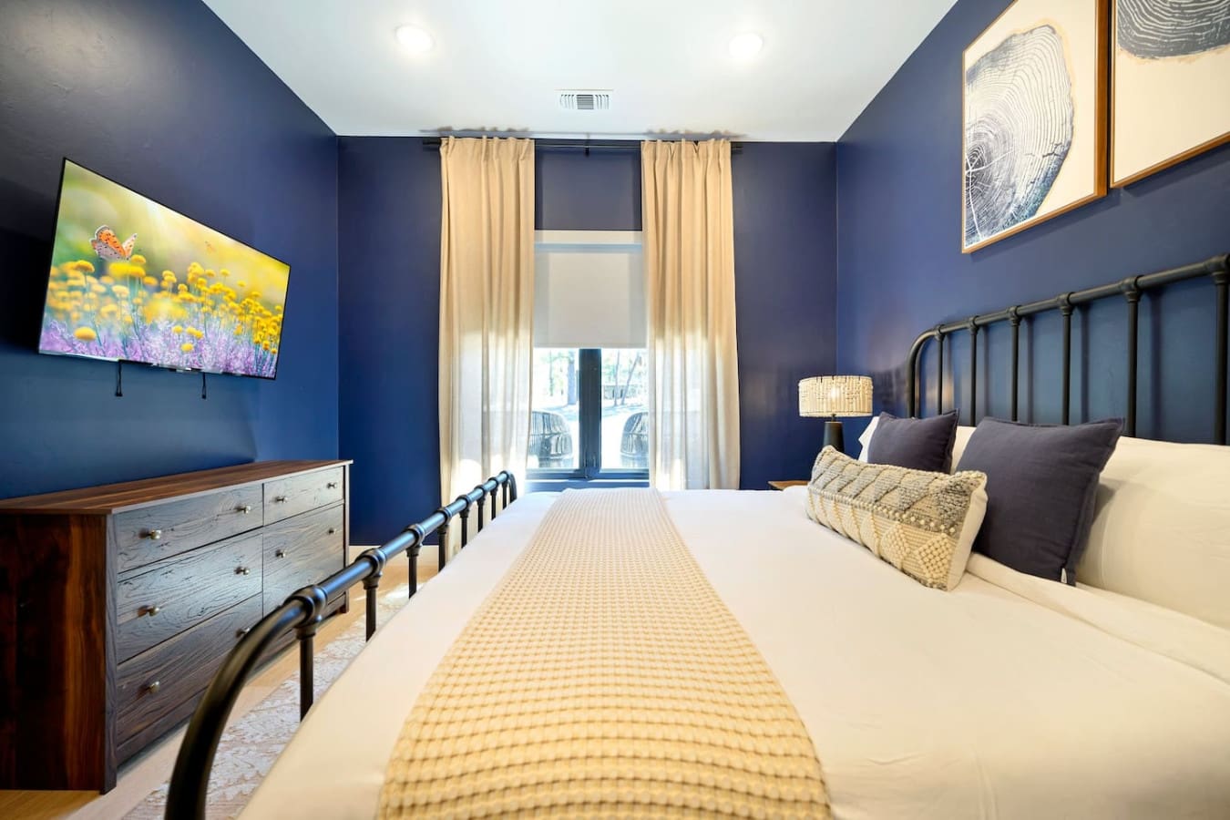 This bedroom is basically a moody dream with those rich navy walls, sleek black metal bed frame, warm gold accents, and those gorgeous tree-ring art prints that make you feel like you're sleeping in a sophisticated forest sanctuary.