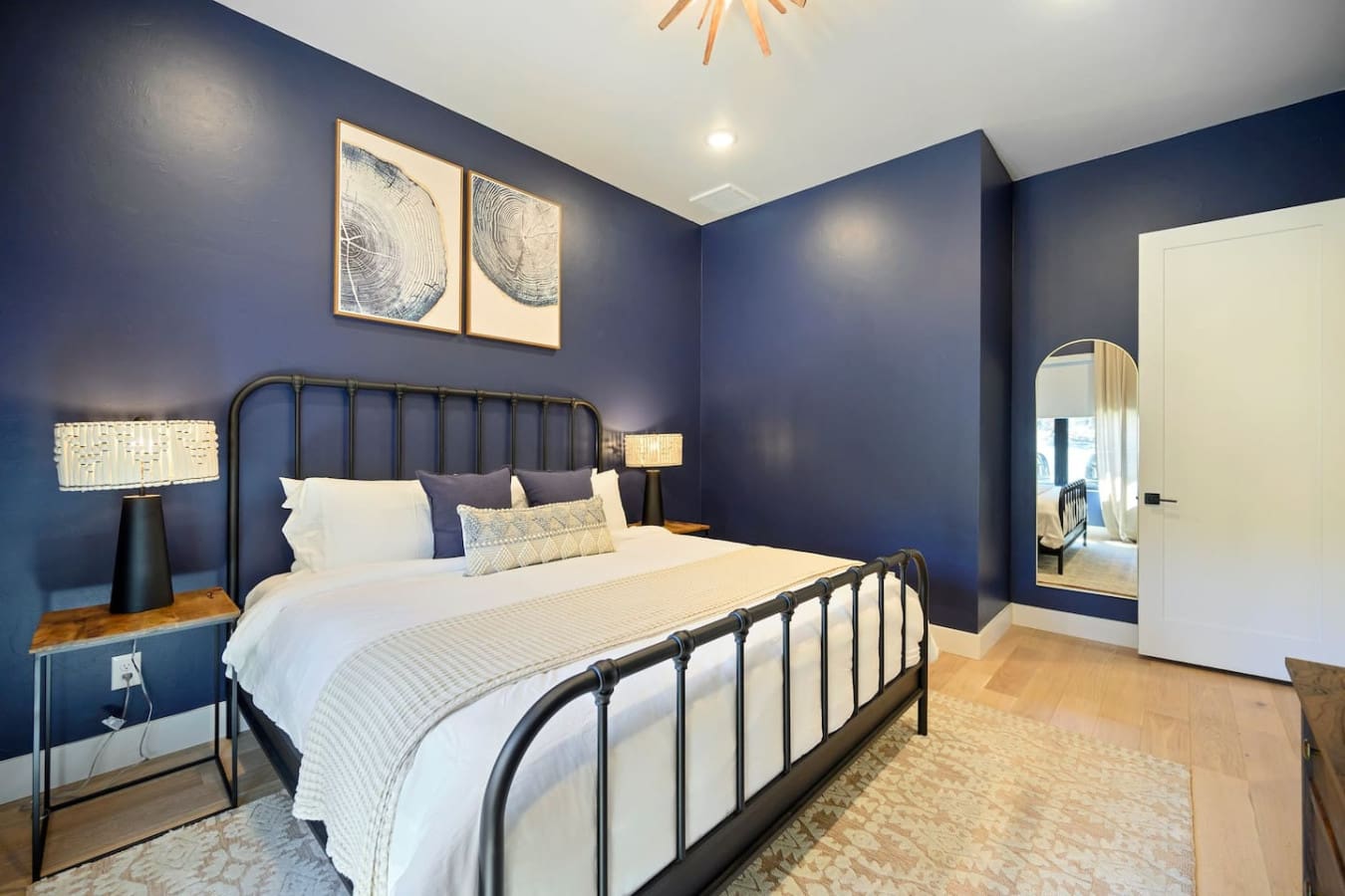 This bedroom is basically the ultimate cozy retreat with those rich navy walls, sleek black metal bed frame, warm gold accents, and those cool tree-ring art prints that tie the whole forest-escape vibe together perfectly.