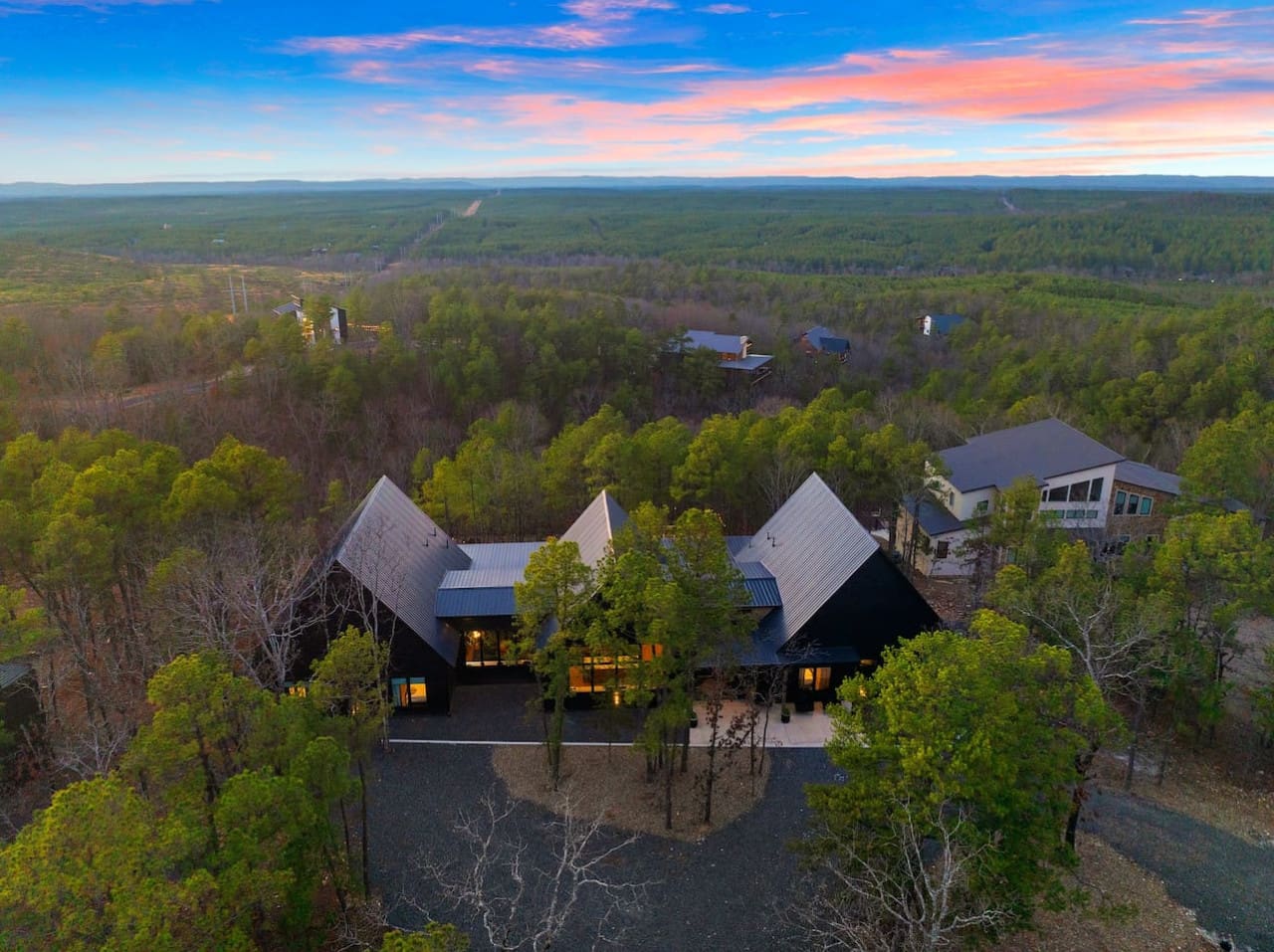 From this dramatic modern hideaway perched among the pines, you're basically looking out at a endless forest that stretches all the way to the mountains, with that insane sunset sky painting everything in shades of pink and gold—the kind of view that make