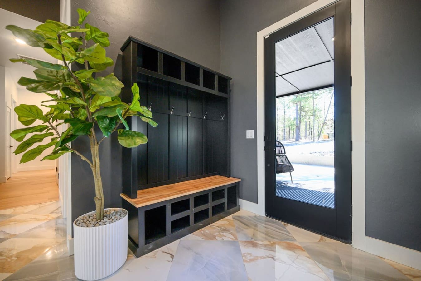 This mudroom setup with the sleek black built-ins, warm wood bench, and those big glass doors framing the forest view is basically the perfect transition space between the cozy interior and the great outdoors.