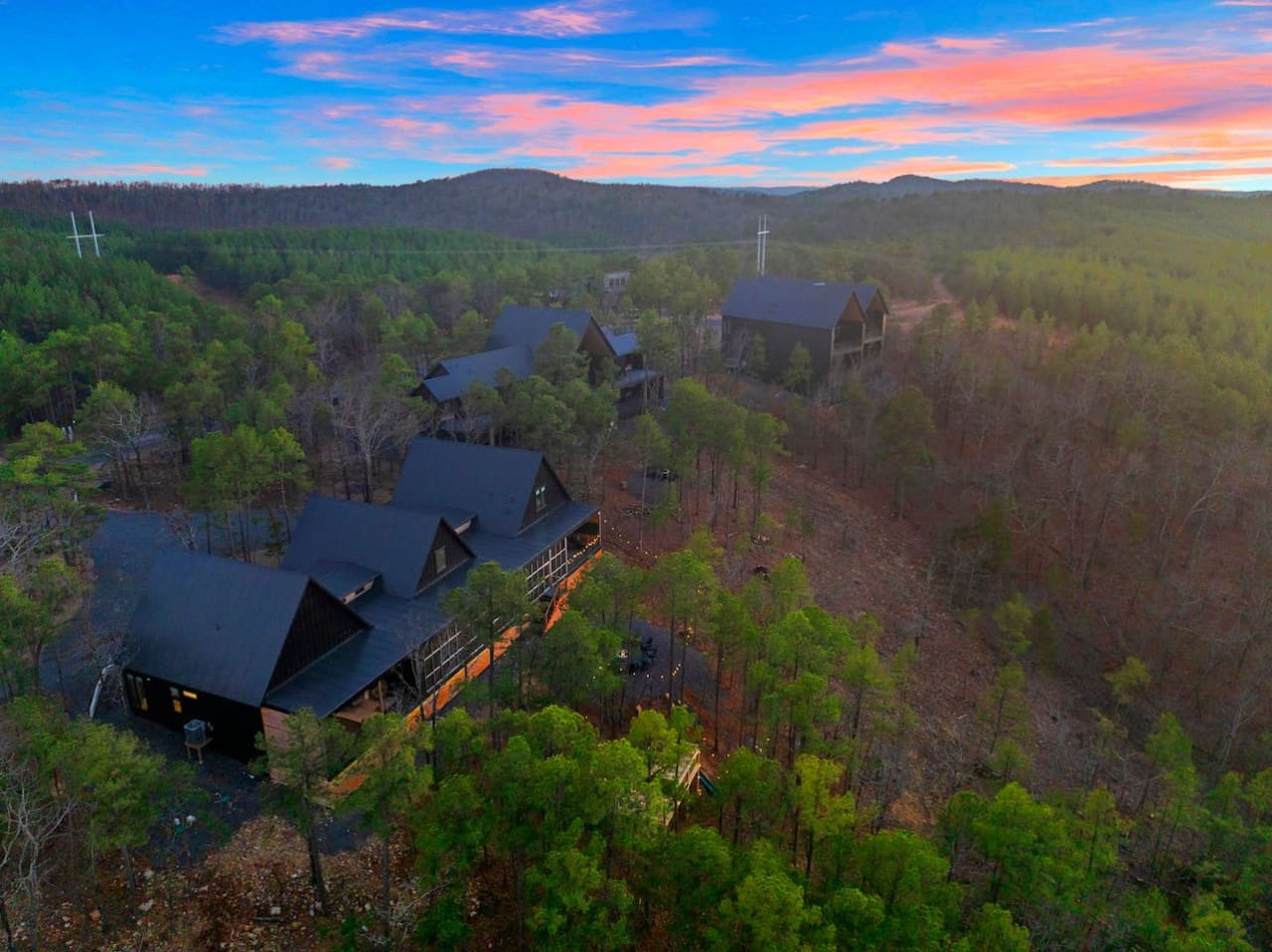 This sprawling modern compound tucked into the forest with those striking peaked roofs and glowing windows basically looks like the ultimate retreat where you can watch the sunset set the sky on fire from multiple angles while surrounded by endless pine-c