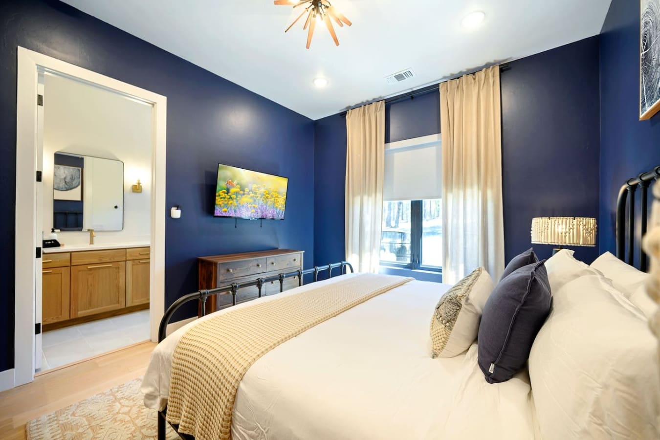 This primary suite is basically the perfect blend of sophisticated and cozy—deep navy walls, crisp white bedding, a spa-like ensuite just steps away, and those floor-to-ceiling windows letting you wake up to the forest views.