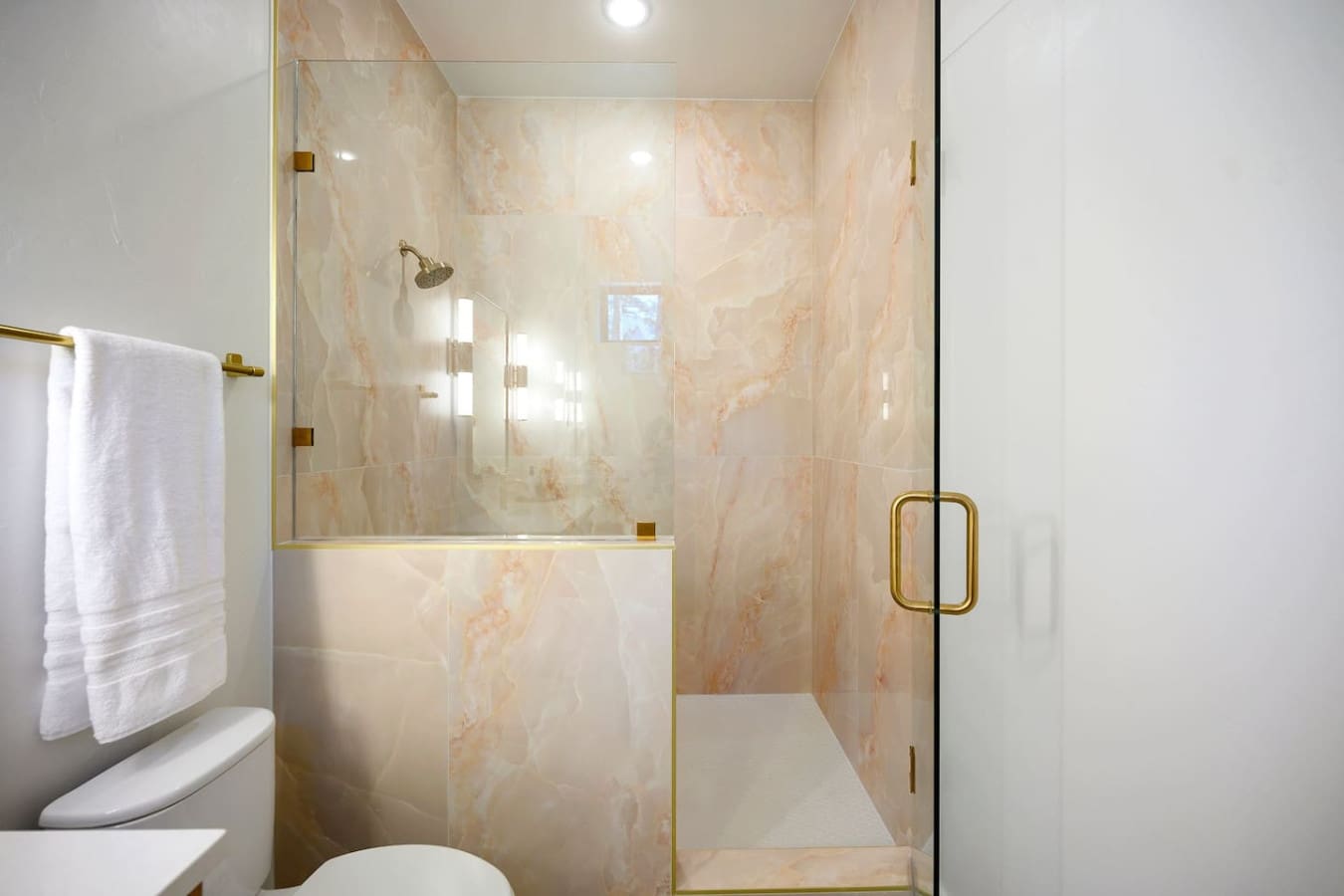 This marble-look shower with its warm peachy tones, brass rainfall showerhead, and that gorgeous frameless glass enclosure is basically the kind of space that makes you want to turn your morning routine into a full spa experience.