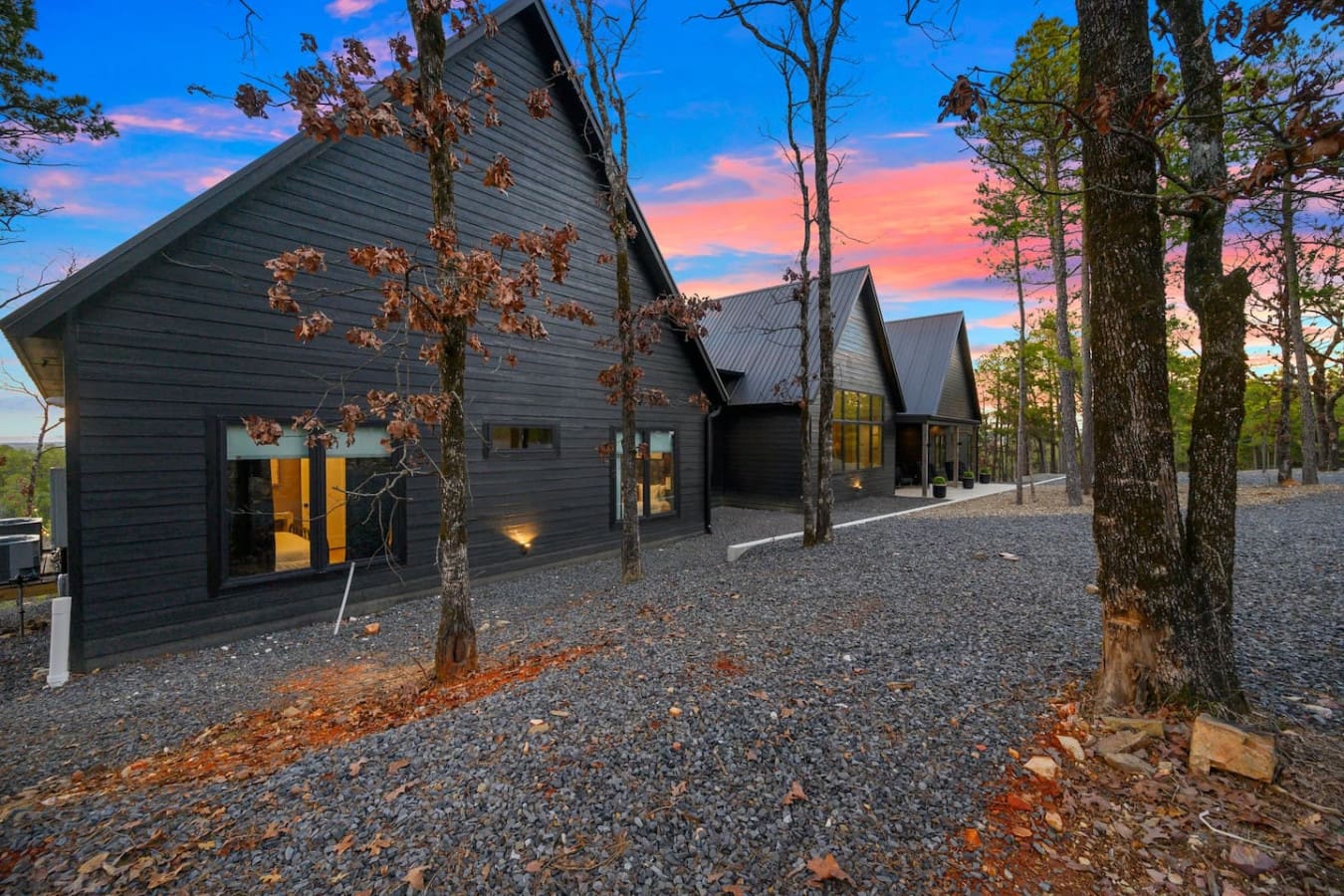These modern barn-style structures nestled among the tall pines with their dramatic peaked roofs and warm glowing windows basically feel like discovering a hidden architectural gem where contemporary design and forest tranquility somehow just work togethe