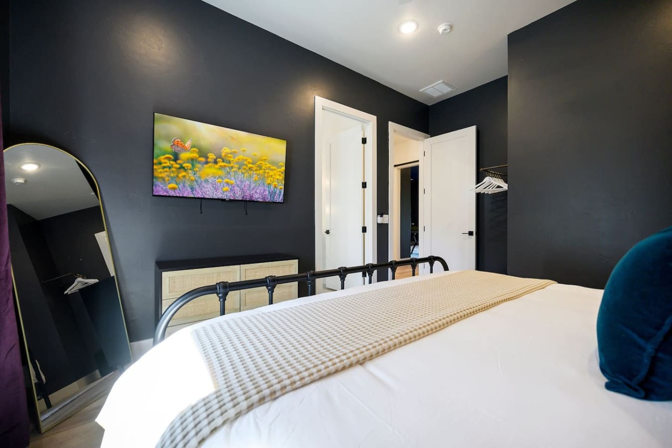 This modern bedroom hits that sweet spot between sleek and cozy with its dark moody walls, that bright colorful landscape art, and crisp white bedding that just makes you want to dive in.