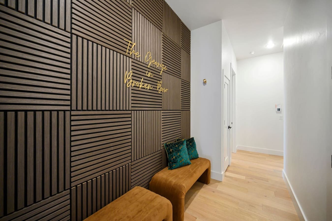 The entryway's geometric wood accent wall with that glowing gold neon sign basically gives you all the design energy you need to know this place is going to be special.