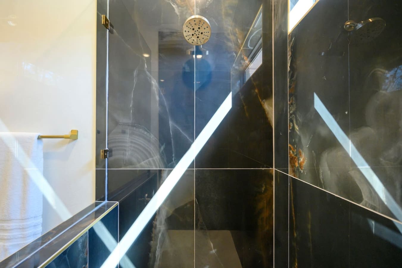 This sleek walk-in shower with its frameless black glass doors, rainfall showerhead, and those dramatic dark tile walls is basically the kind of space that makes you actually look forward to your morning routine.