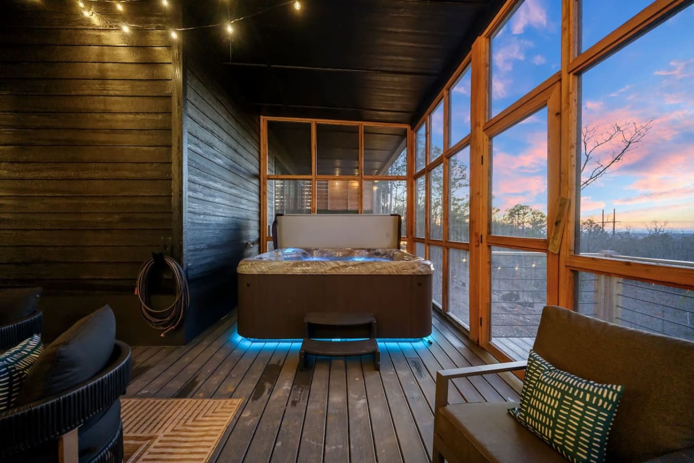 This hot tub with the glowing blue underlit base and those massive windows framing the sunset sky is basically the ultimate way to end your day—soak in the warmth while watching the clouds turn pink and orange over the treetops.