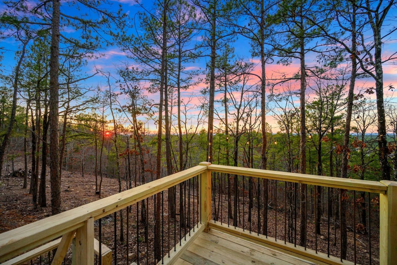 Imagine settling onto this wood deck with that stunning sunset blazing through the trees—basically the kind of view that makes you forget your phone exists and just sit there watching the sky turn pink and gold over endless forest.