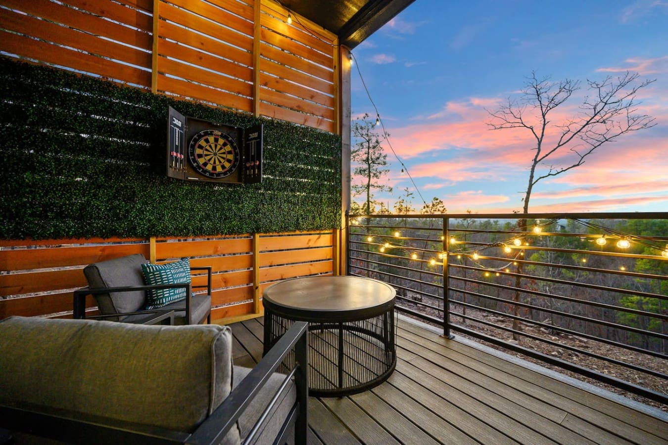This covered deck is basically your own private sky lounge—string lights twinkling overhead, a cozy fire pit setup, that electronic dartboard for some friendly competition, and a sunset view that's honestly almost too beautiful to look away from.