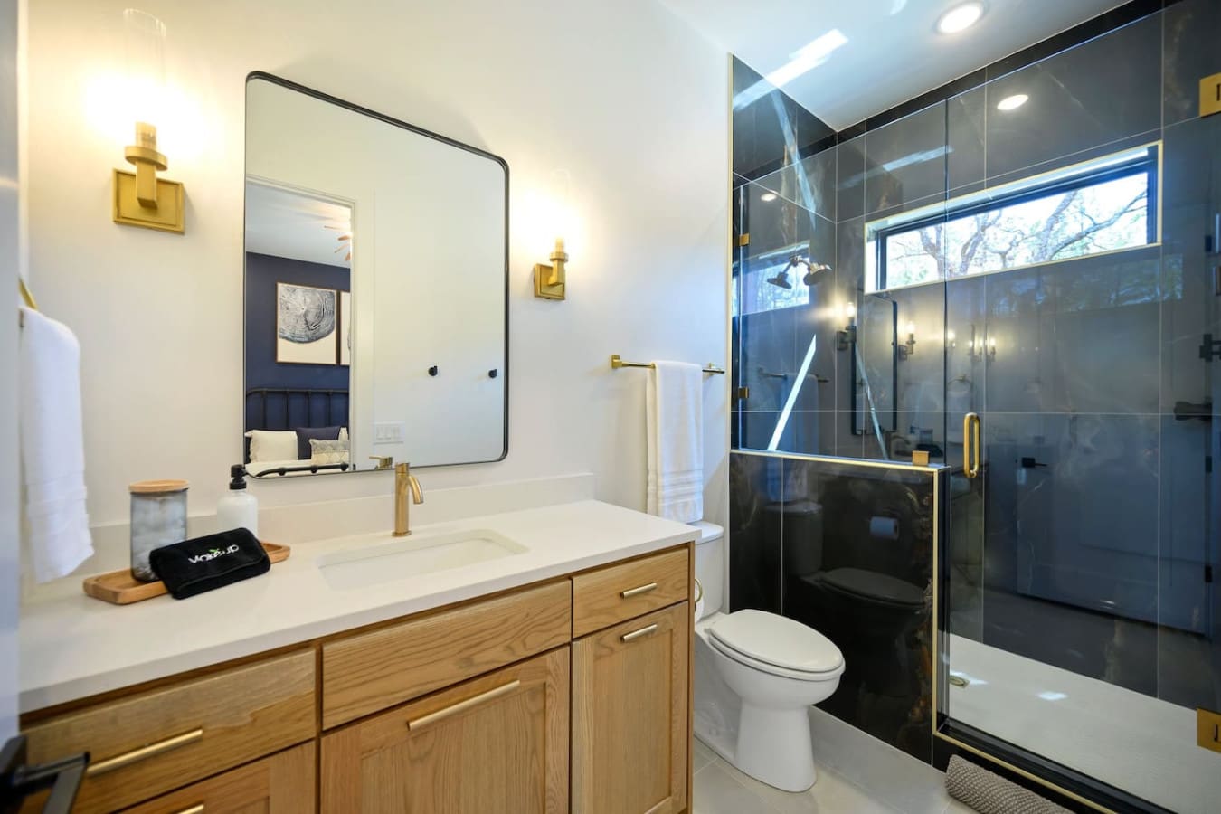 This spa-like primary bathroom is basically a total dream with that gorgeous walk-in shower framed by black glass, warm wood vanity, elegant brass fixtures, and those skylight windows letting natural light flood in while you get ready.