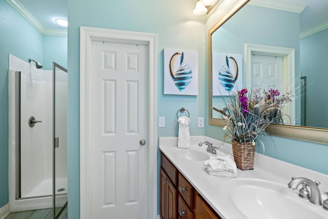 This guest bathroom is basically a little turquoise sanctuary with everything you need—dual sinks so nobody's fighting over counter space, those adorable feather artworks that scream coastal vibes, and fresh flowers that somehow make washing your hands fe