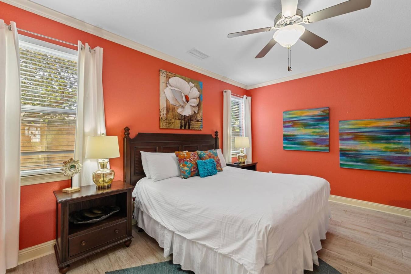 This vibrant coral bedroom is basically where good design meets serious comfort—bold walls, colorful art that actually makes you smile, and a dark wood bed that's somehow the perfect anchor for all that tropical energy.