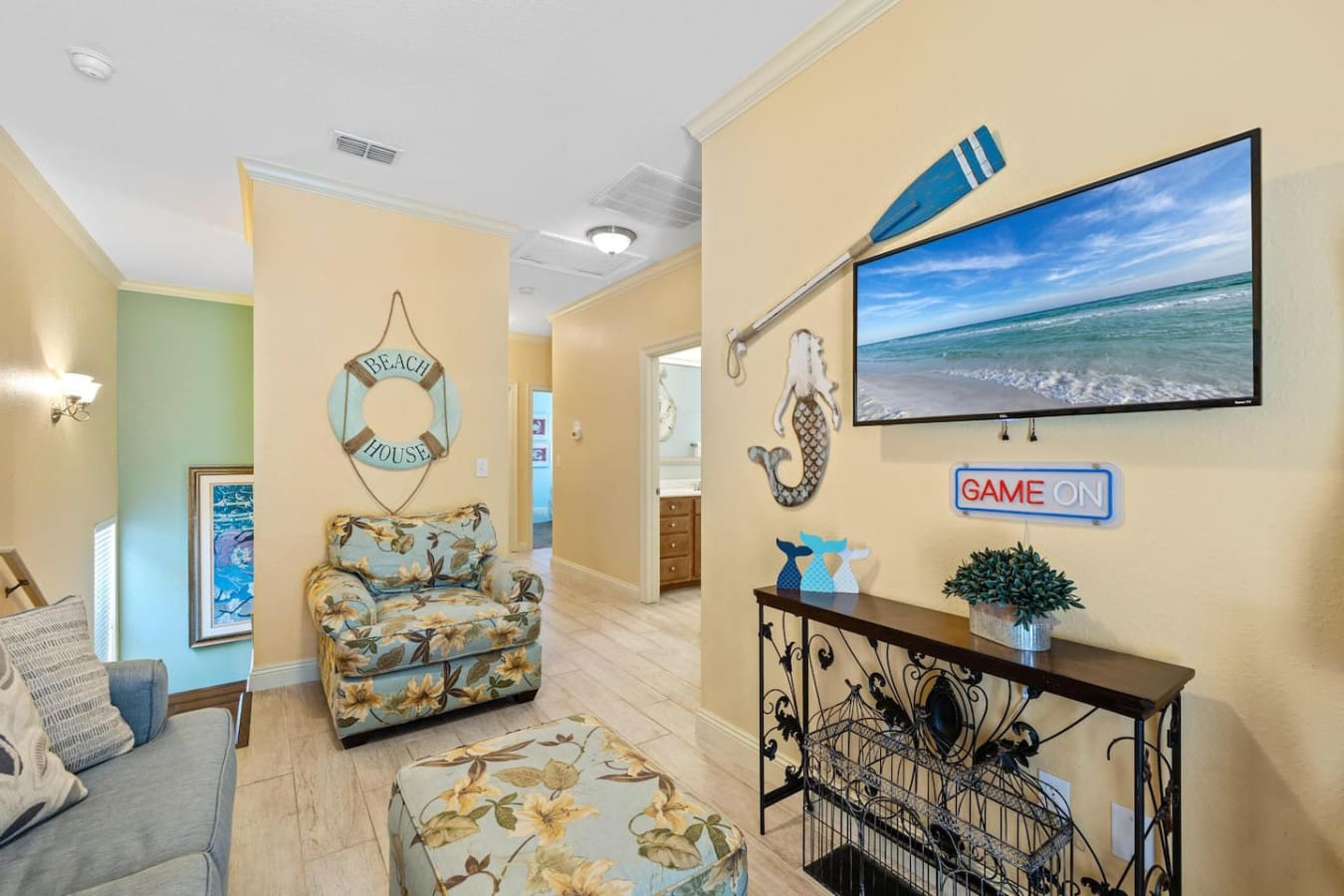 This cozy living room proves you don't need to actually be at the beach to feel like you're living the dream—the view's right there on the screen, the games are stacked and ready, and that "Game On" neon sign basically gives you permission to embrace your