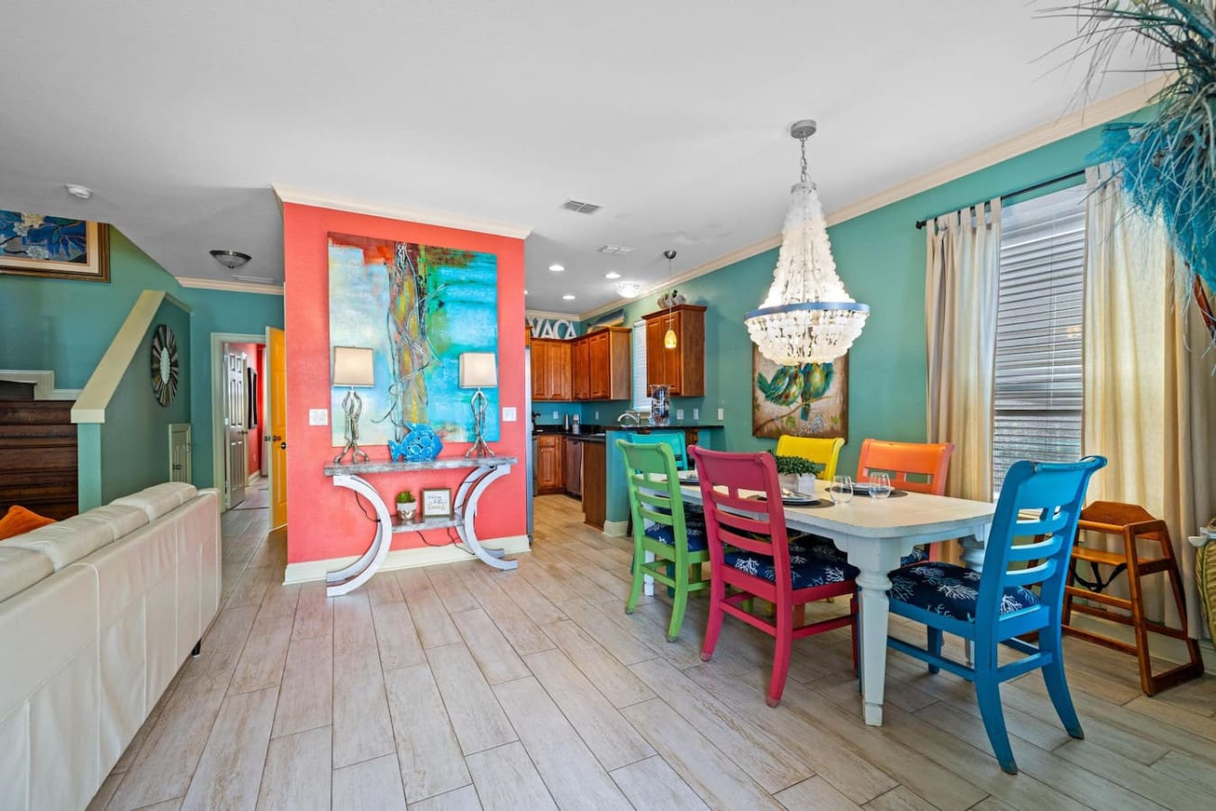 This open-concept living space is basically a masterclass in playful color—where turquoise walls, a coral accent kitchen, and rainbow dining chairs come together to prove that vacation homes don't have to choose between stylish and fun.