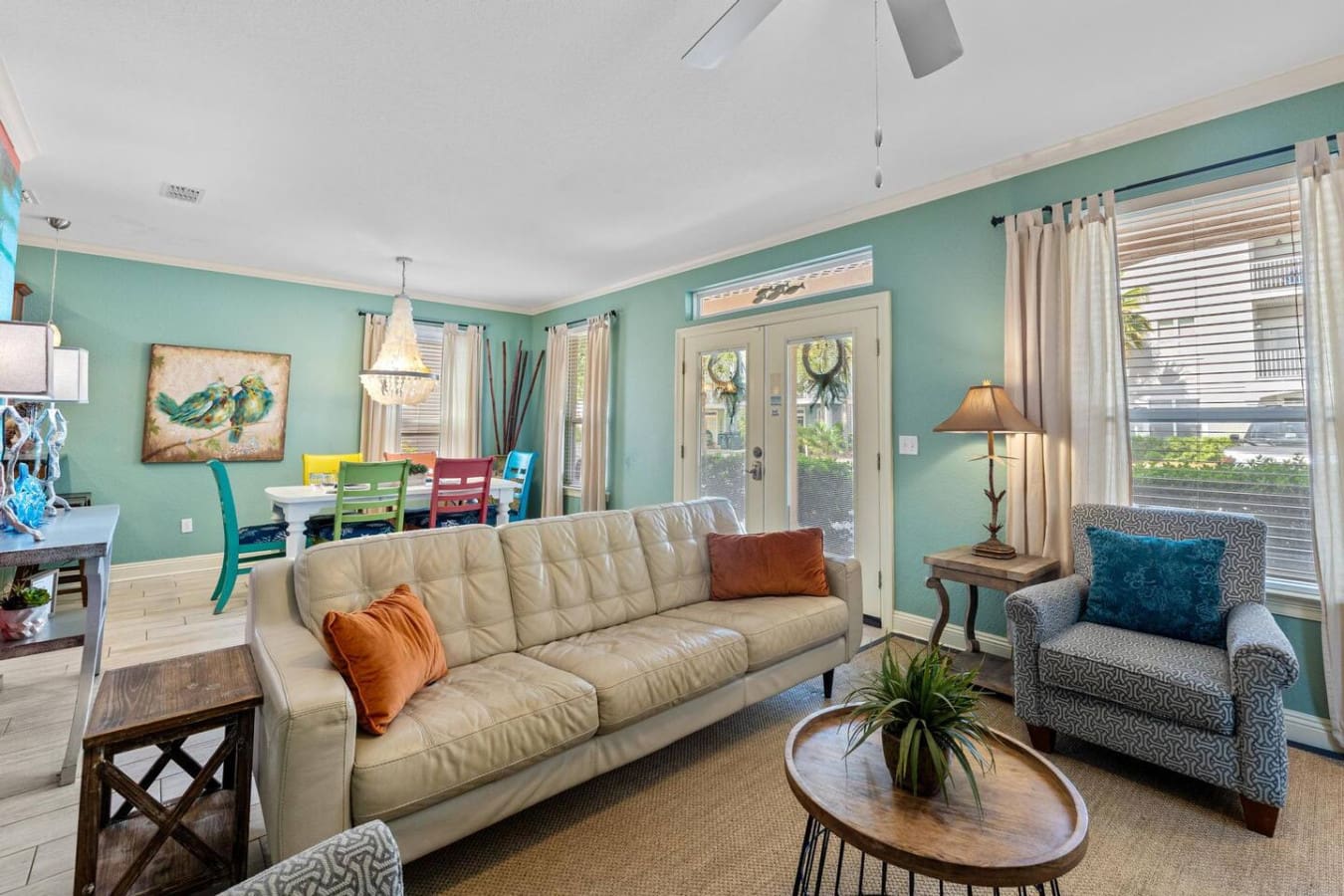 The living room is basically your invitation to settle in for the long haul—cream sofa, cozy chair, that perfect little round table, and those turquoise walls wrapping around you like a warm hug that somehow feels like the beach without ever leaving your