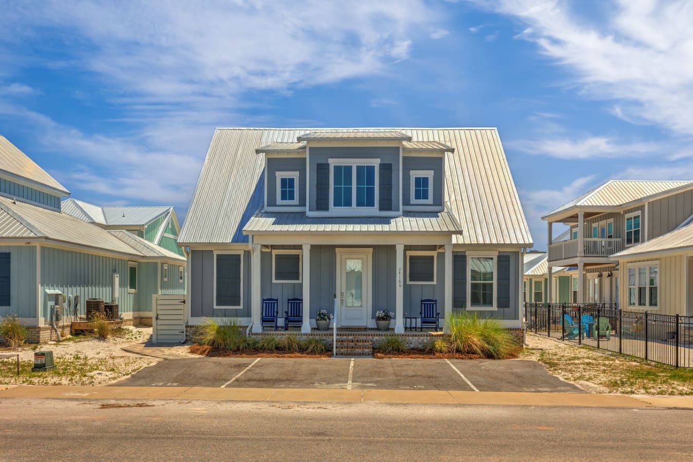 This modern coastal home is giving serious beachy vibes with that crisp two-story design, metal roof, and those blue rockers on the porch just waiting for you to kick back and relax.
