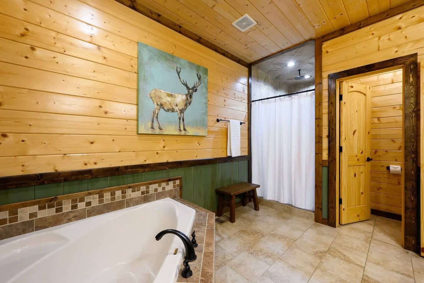 This master bath is where you get the whole cabin experience—a deep soaking tub, a walk-in shower, natural wood everywhere, and that deer painting watching over you like you're in your own private lodge.