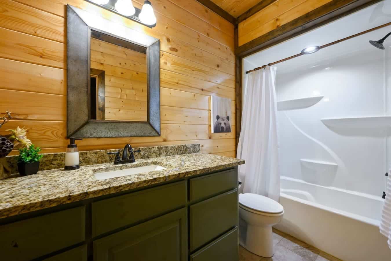 This master bathroom's got the rustic cabin aesthetic dialed in with wood walls everywhere, a granite countertop that actually has space to set stuff down, and a mirror that doesn't make you feel like you're squinting at yourself.