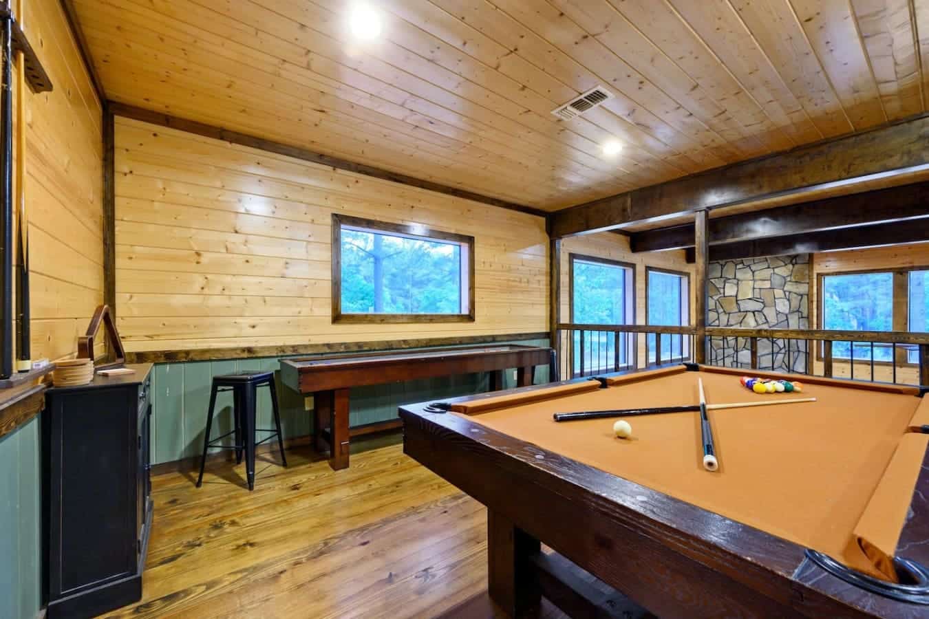 This game room's got enough going on—pool table, bar seating, stone fireplace—that you could genuinely hang out here all day without feeling like you're missing the actual cabin.