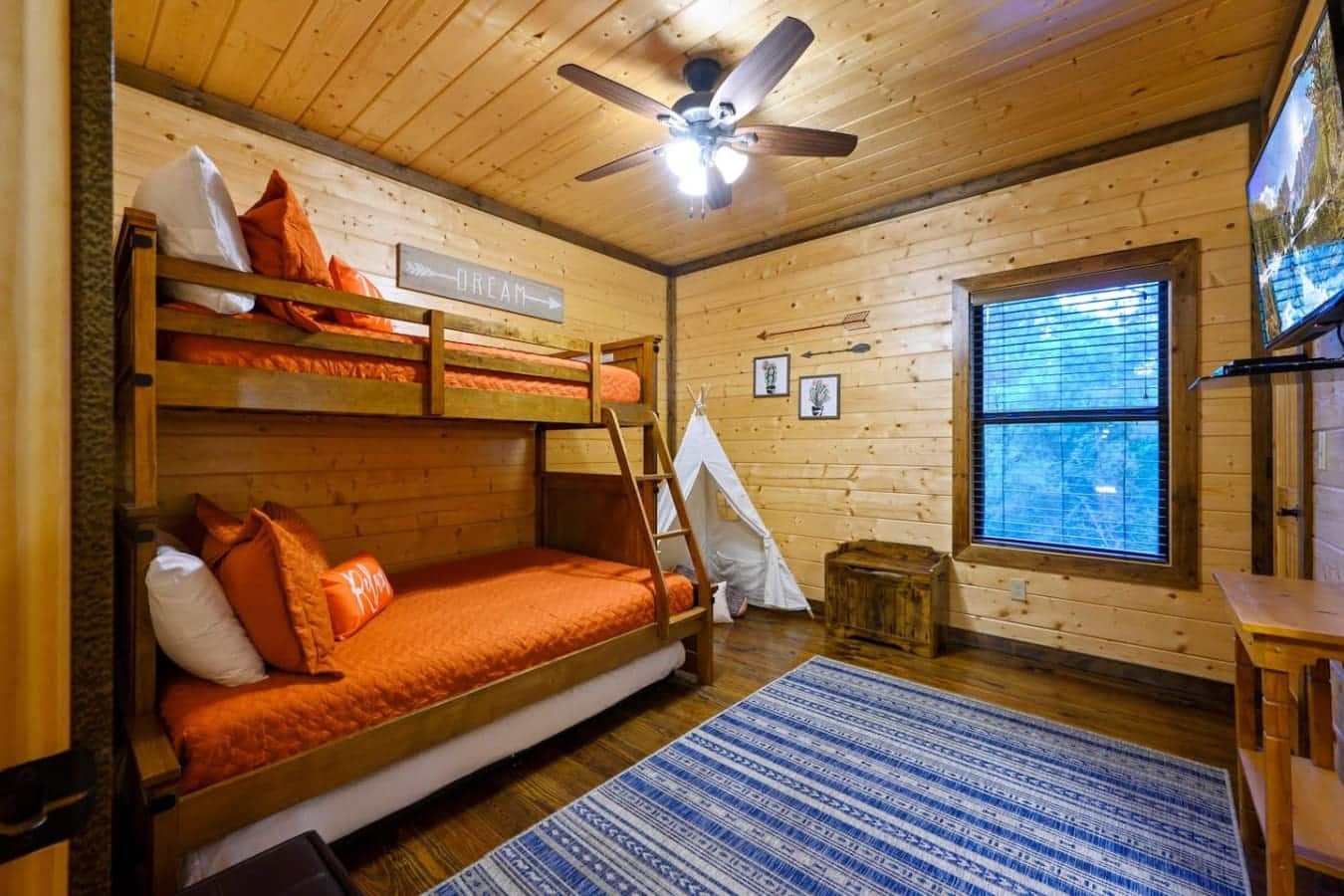 This kids' room's got bunk beds with actual comfortable mattresses, a little teepee situation for when someone needs their own space, and enough orange bedding to make sure nobody's ever confused about whose stuff is whose.
