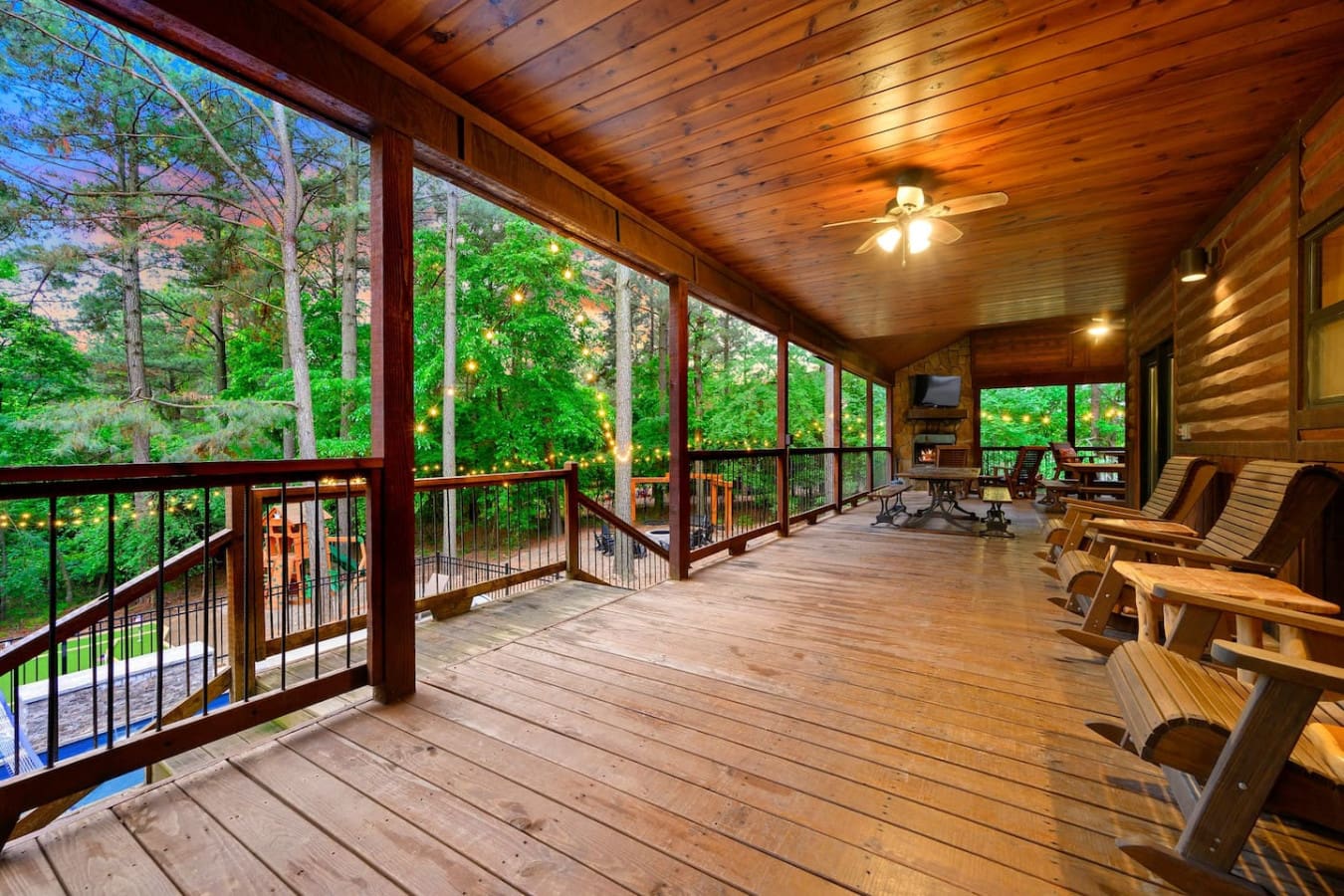 This screened porch is basically built for hanging out—it's got the ceiling fans, the warm lighting, the crazy amount of windows looking out at all those trees, and enough space that your whole group can actually stretch out and not feel like you're on to