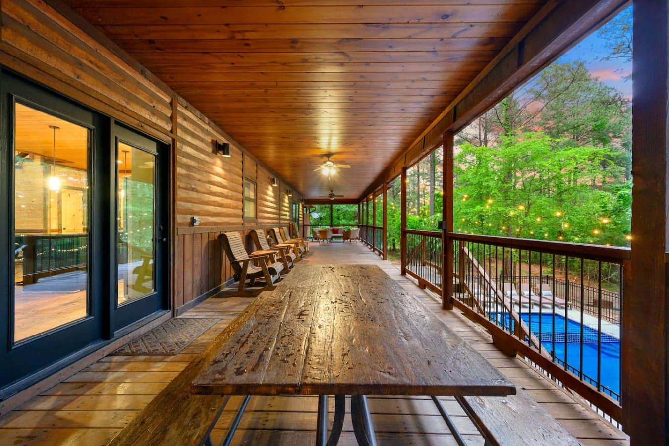 This covered porch basically never stops—it's got the whole wraparound vibe, a massive table for gathering, and all those windows framing the trees so perfectly that you'll wonder why anyone ever eats inside.
