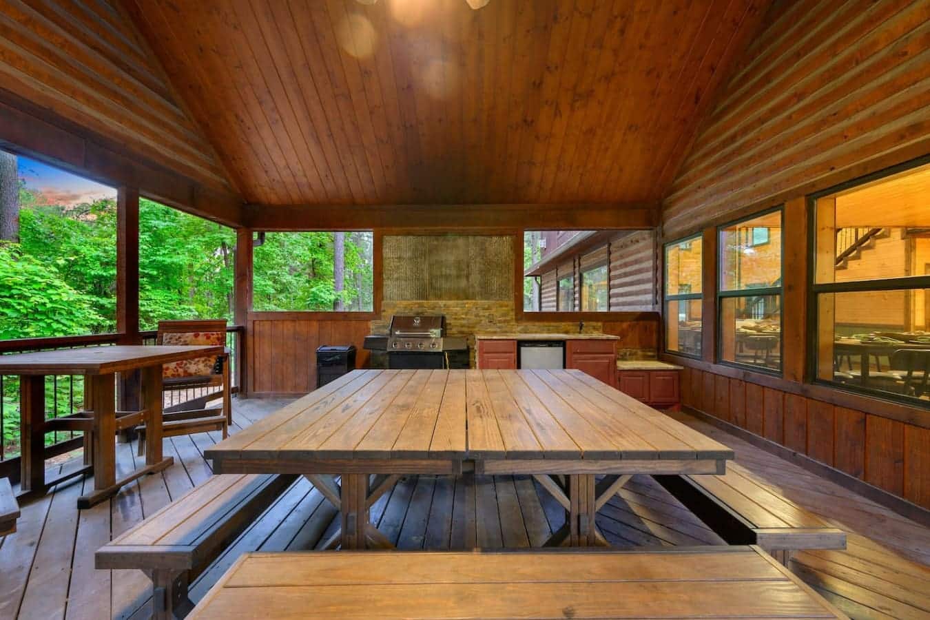 This screened porch is basically your whole vacation right here—huge wooden tables, wood ceiling overhead, windows on every side, and enough room to spread out and actually live in the space for days.