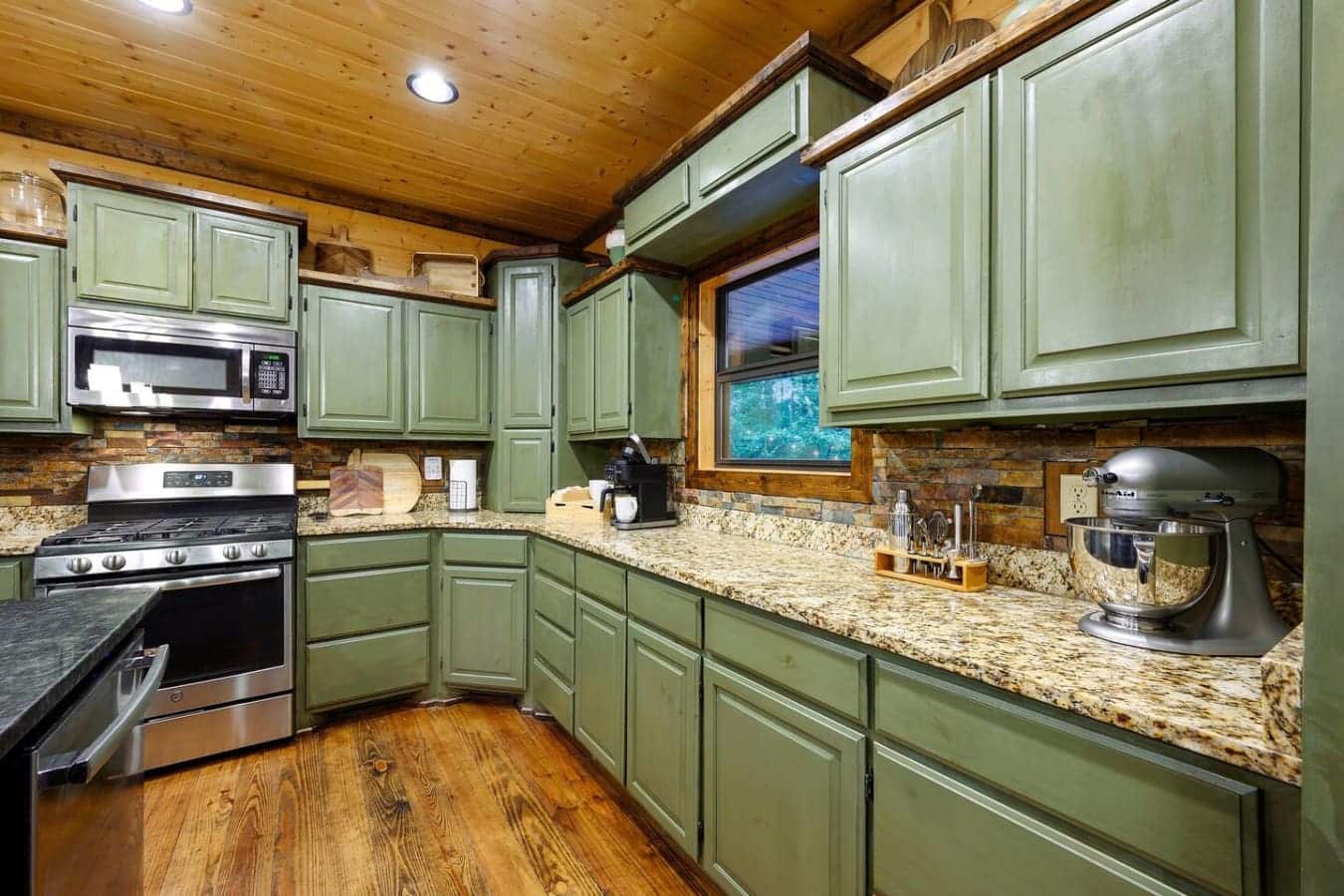 This kitchen's got the green cabinets, granite counters, and wood-beam ceilings that make you feel like you're cooking in a fancy cabin instead of just heating up leftovers.