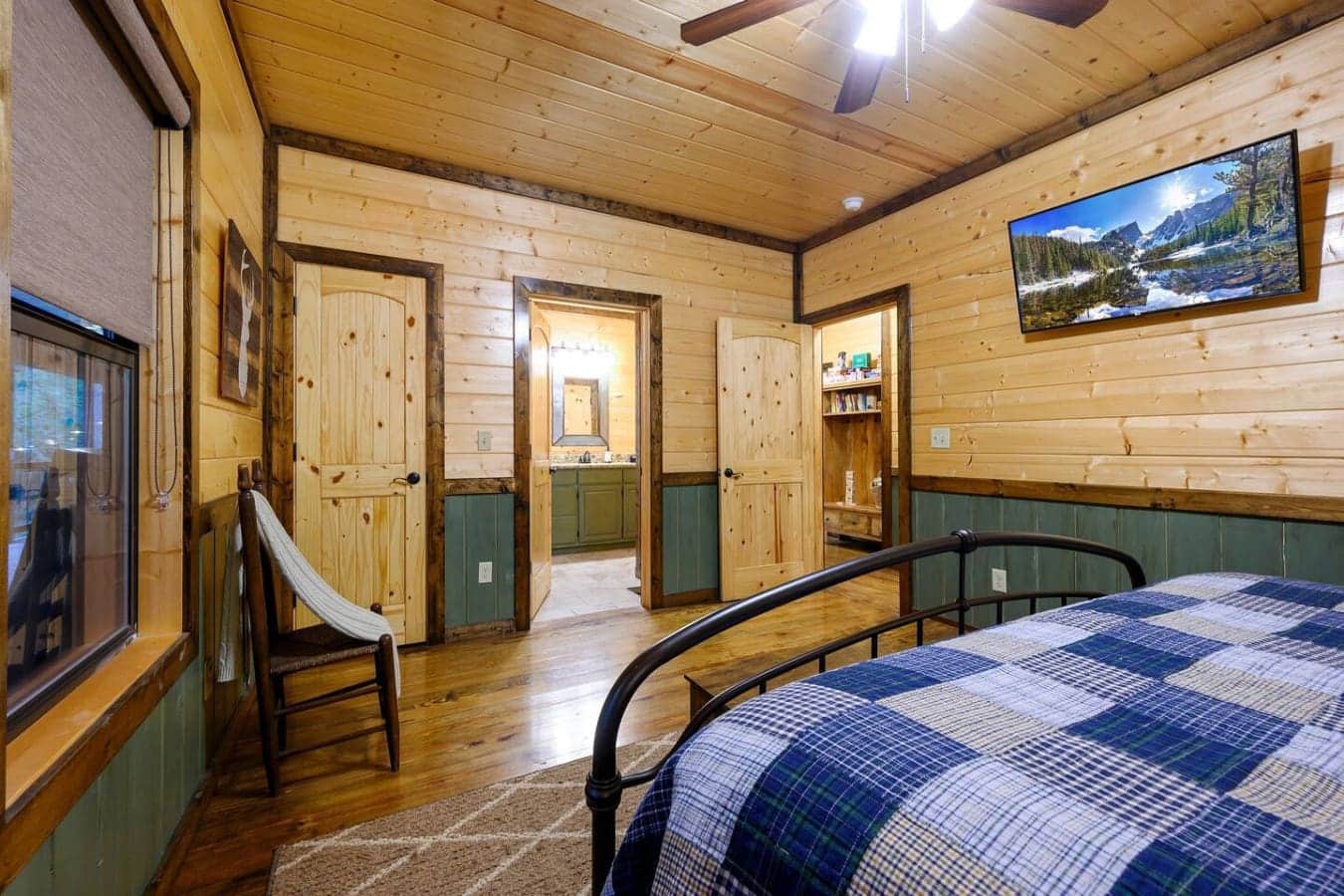 This master suite feels like your own private cabin retreat with the wood-beamed ceiling, plaid bedding, and those big windows letting you wake up to the forest views without having to leave bed.