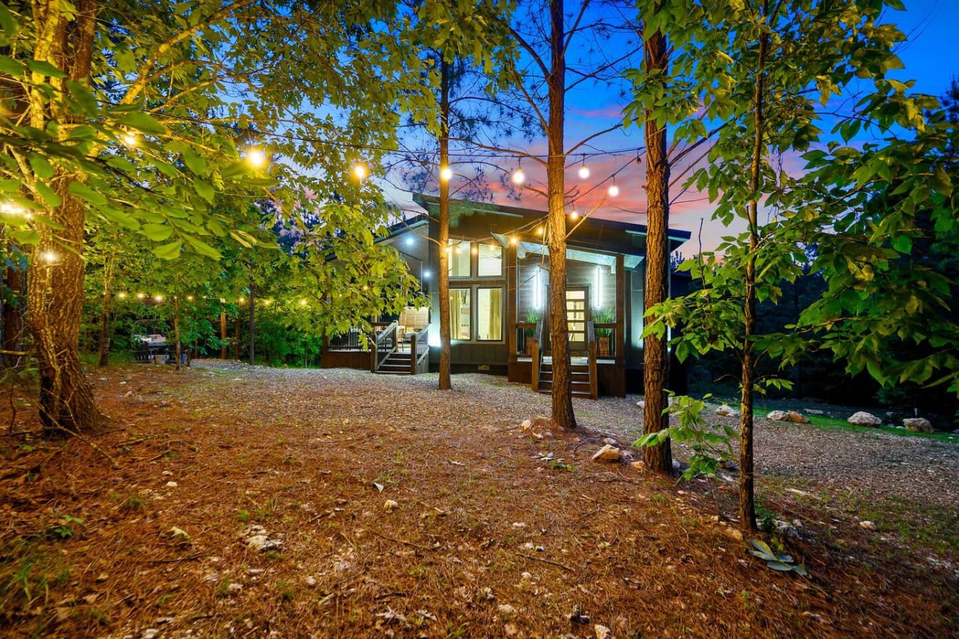 This modern cabin feels like your own glowing sanctuary nestled deep in the pines—surrounded by towering trees and twinkling lights as the sky shifts into those perfect twilight colors.