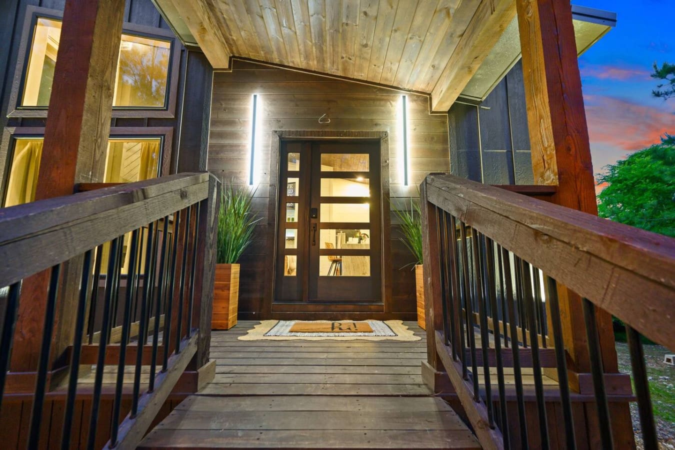 This entrance hits different at twilight—all those warm lights glowing against the dark wood and glass, flanked by those sleek railings, making you feel like you're about to step into your own private sanctuary tucked into the trees.