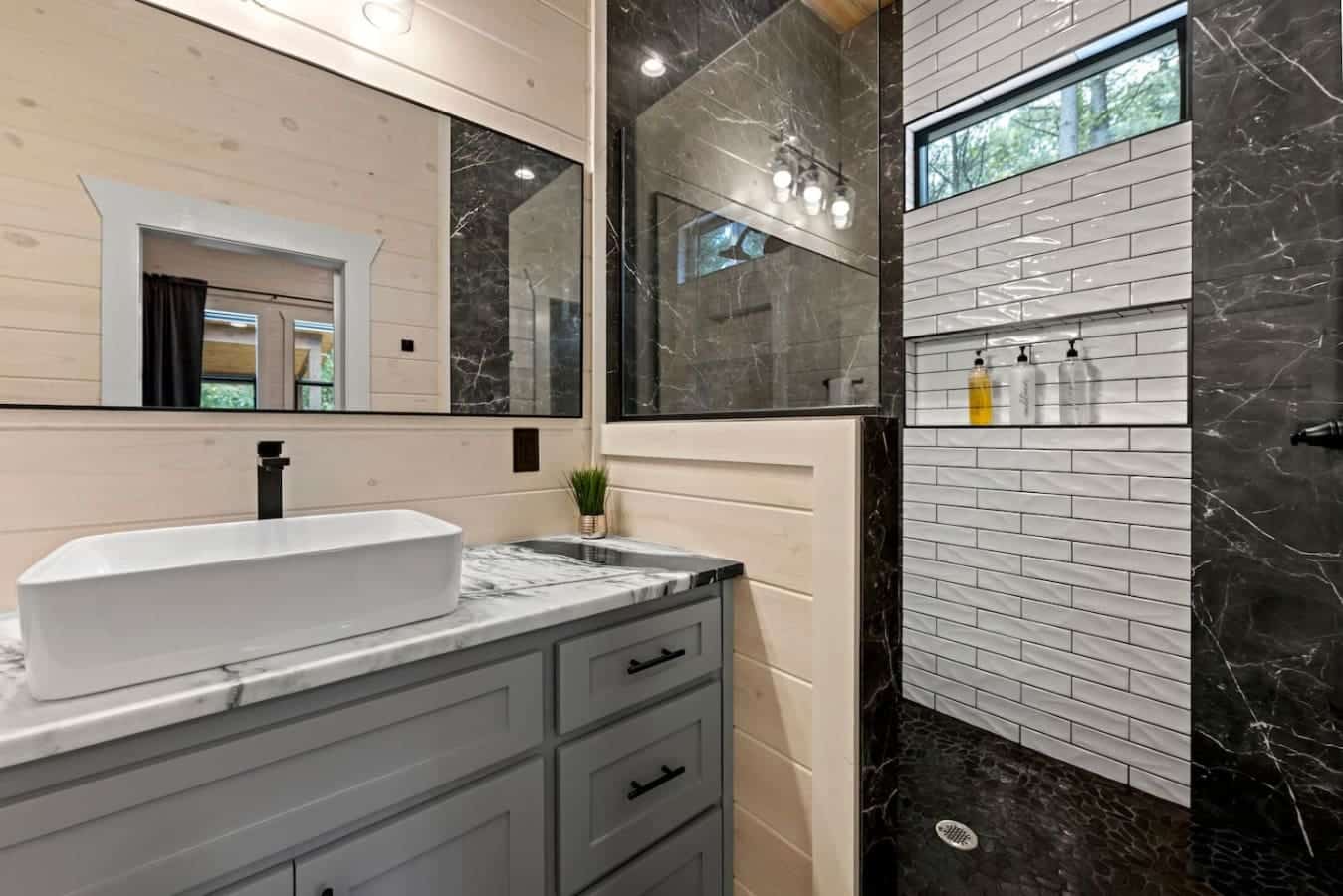 Modern rustic elegance: a sleek vessel sink, marble accents, and bold black finishes bring sophistication to this cozy bathroom retreat.