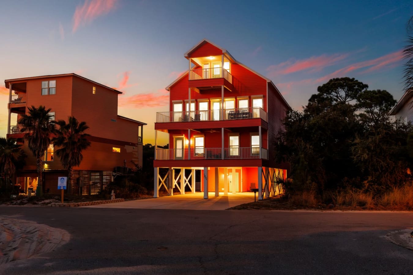 These vibrant beach houses light up like a dream at dusk, and you're staying in the showstopper—that bold red three-story beauty with views for days.