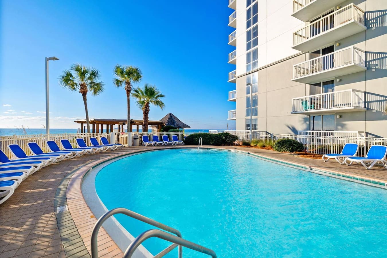 The pool sparkles under endless blue sky, palm trees sway in the breeze, and that ocean beyond feels like it's calling your name—this is the kind of view that makes you never want to leave your lounger.
