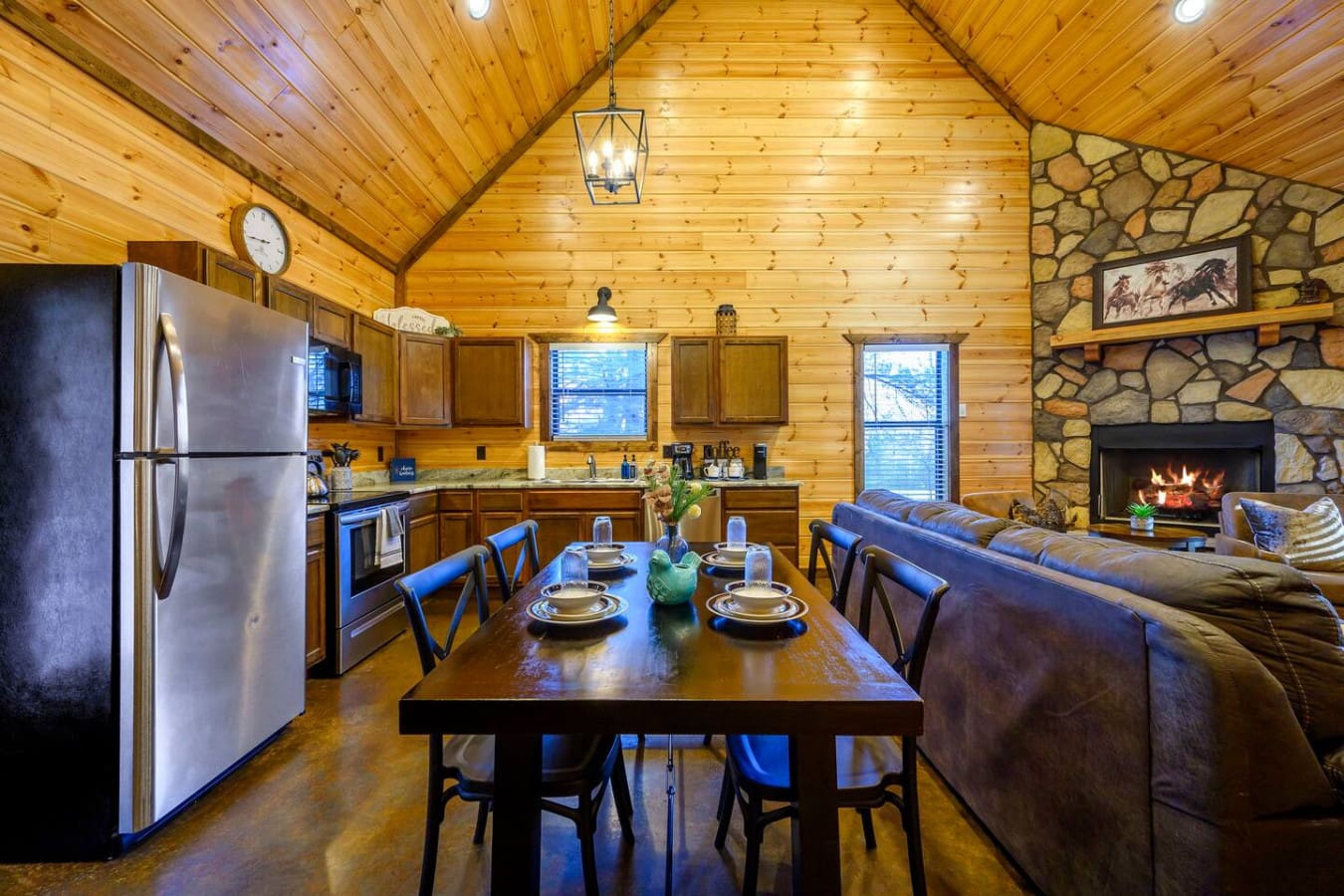 This open-concept cabin feels perfect for gathering with its wood ceilings, stone fireplace, and modern kitchen all in one cozy space.