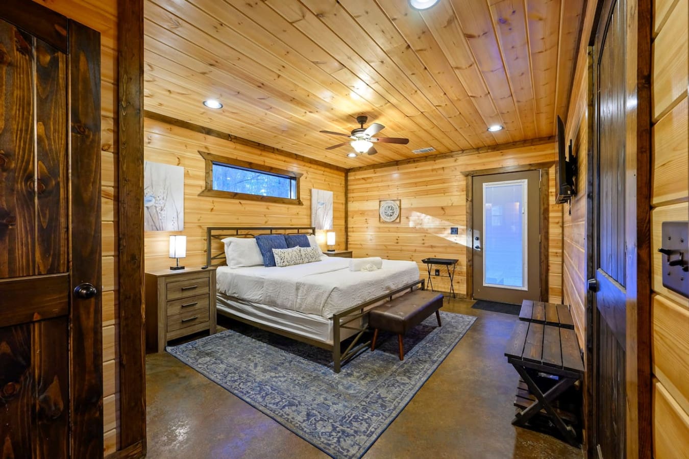 This spacious master bedroom features warm wood throughout, a cozy bed, and direct access to the outdoors.