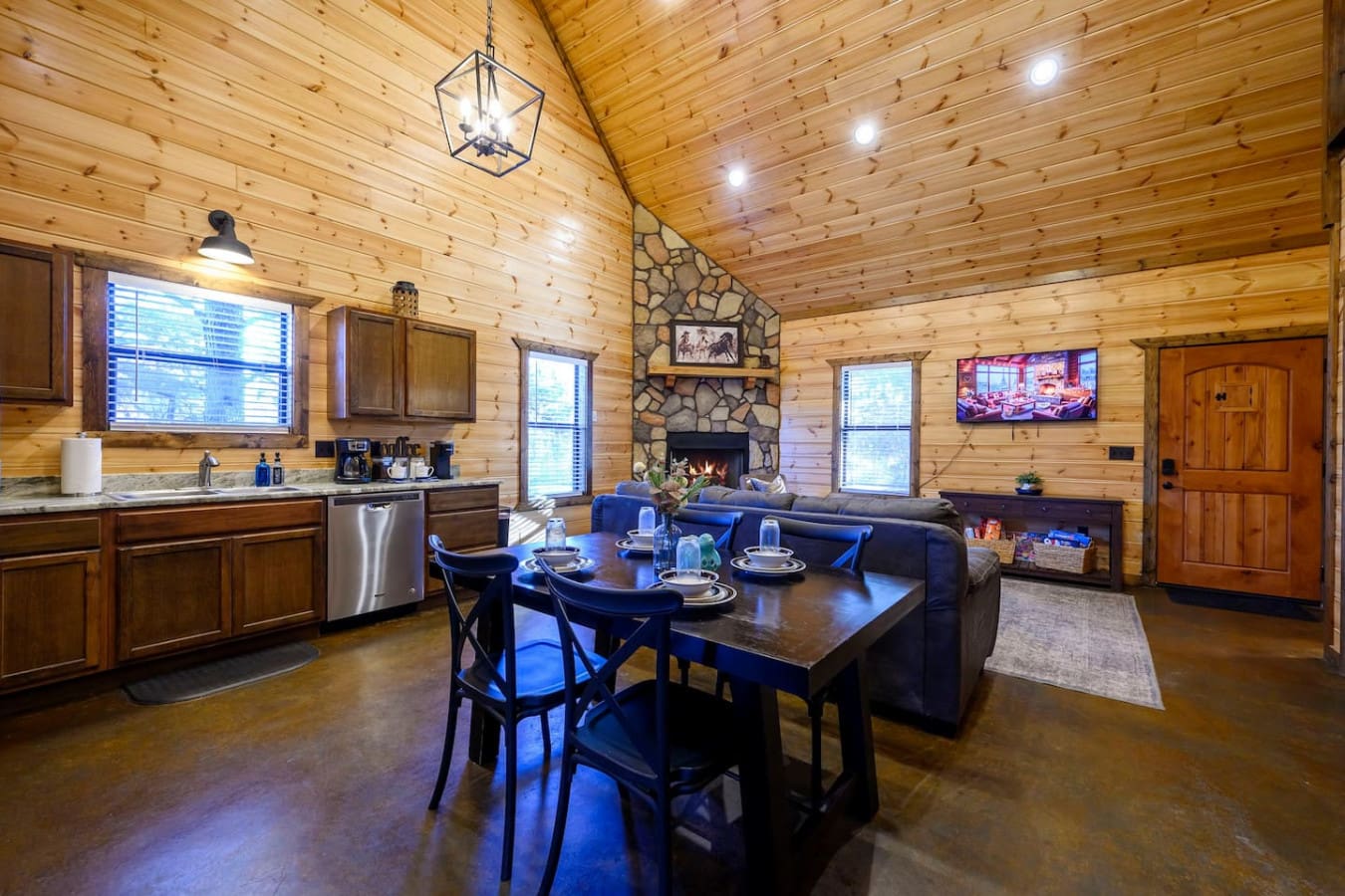 This open-concept cabin features a gorgeous wood-beamed ceiling, stone fireplace, and modern kitchen all in one stunning living space.