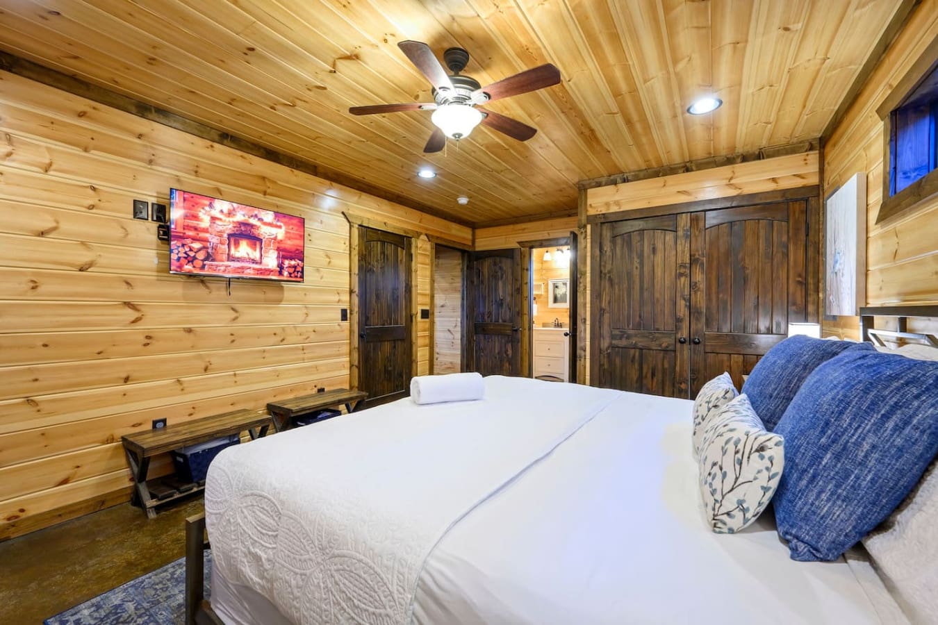 Cozy log cabin bedroom with a king bed, flat-screen TV, and rustic wood finishes throughout.