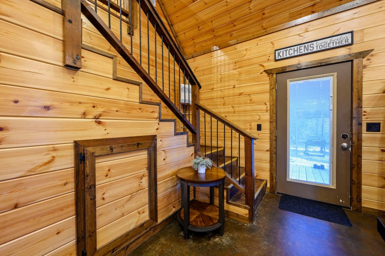 This stunning log cabin entryway features soaring wood ceilings, a dramatic staircase, and gorgeous lake views through the glass doors.