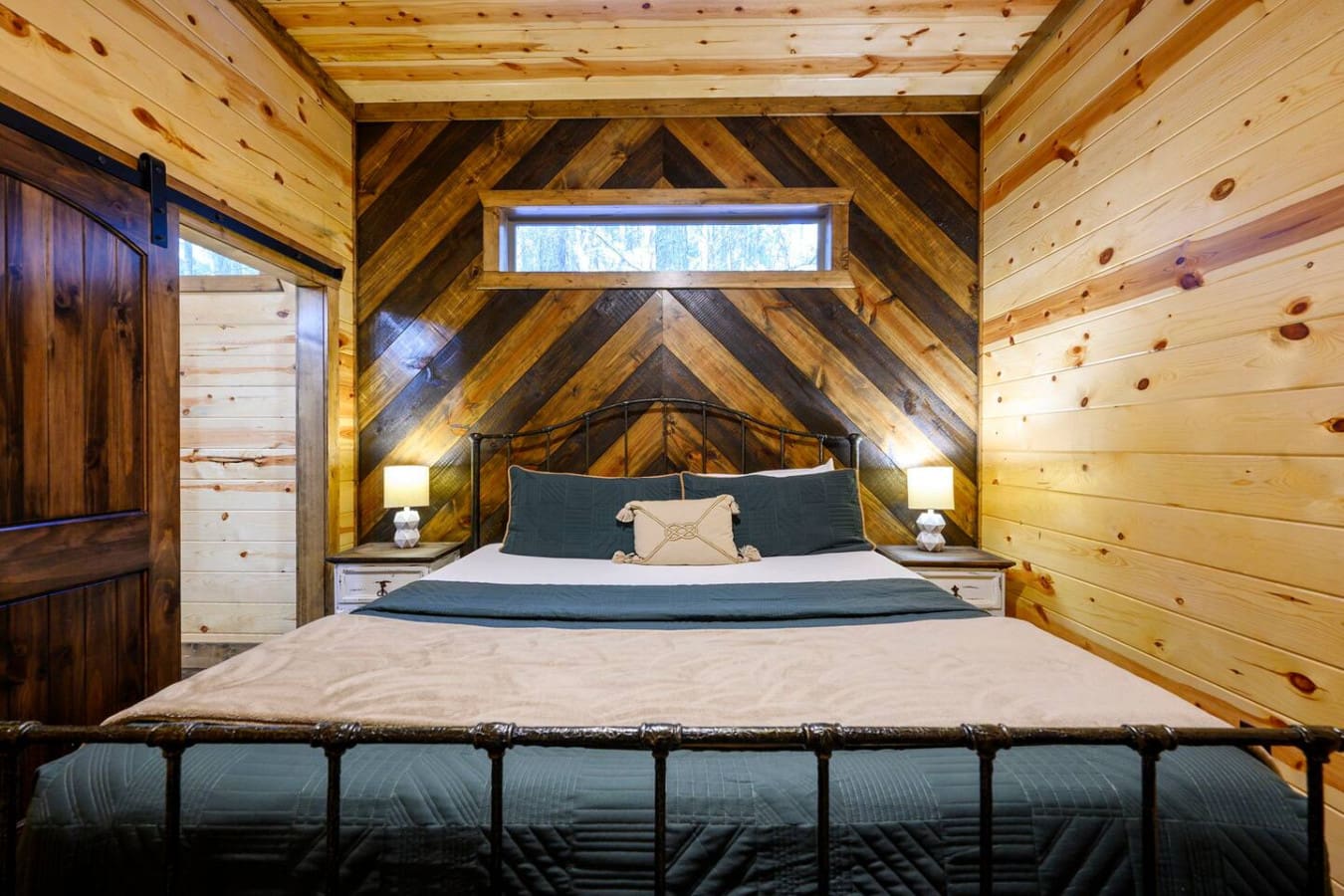 This cozy loft bedroom features soaring exposed beams and a metal bed frame with plenty of natural light from the peak window.