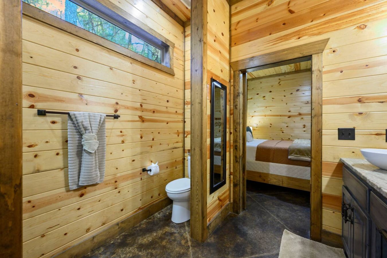 This rustic log cabin bathroom features knotty pine walls, modern fixtures, and direct access to the bedroom suite.