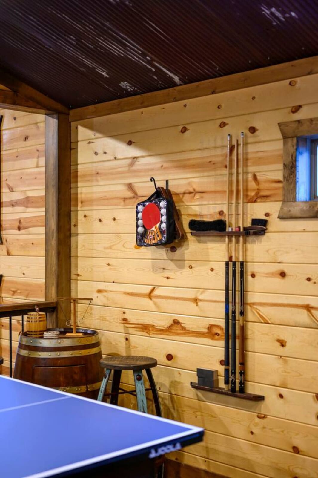 Game room with wooden walls, ping pong table, and wall-mounted storage for sports equipment.