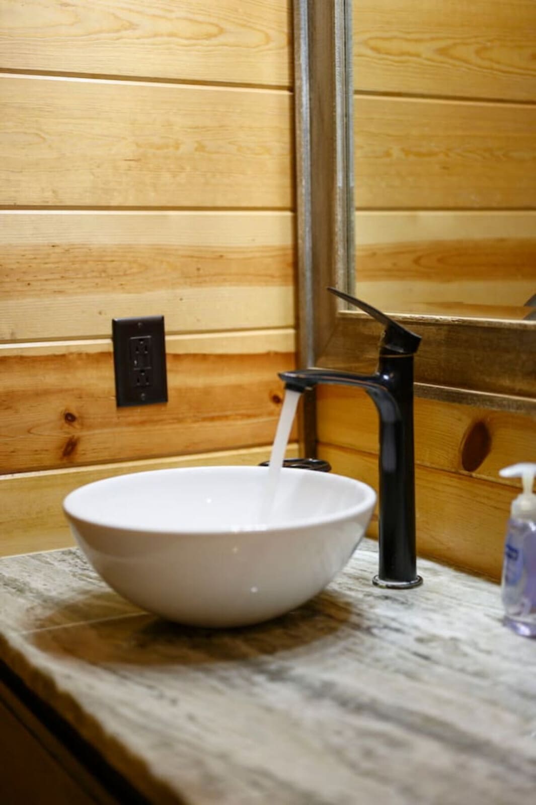 Modern vessel sink with sleek black faucet set against cozy wood-paneled walls in this rustic bathroom.