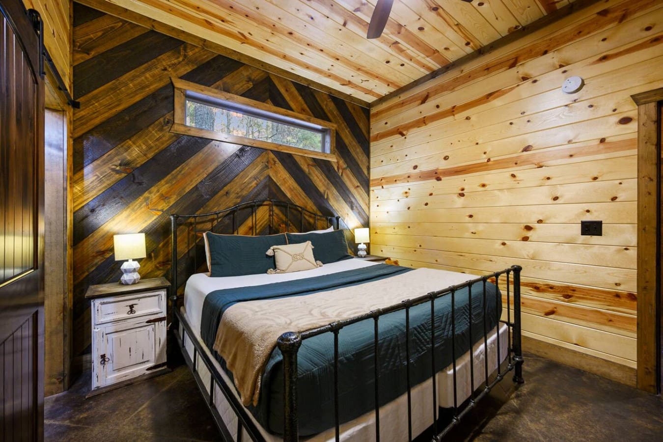 This cozy loft bedroom features exposed wood beams and a metal bed frame with views of the forest outside.