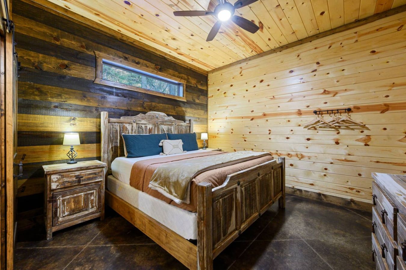 This cozy log cabin bedroom features rustic wood finishes, a comfortable bed, and natural light from the transom window.