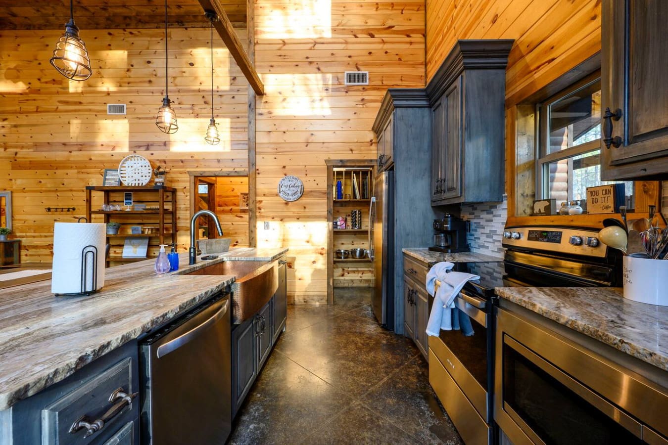 This stunning log cabin kitchen features custom dark cabinetry, stainless steel appliances, and soaring wood ceilings with pendant lighting.